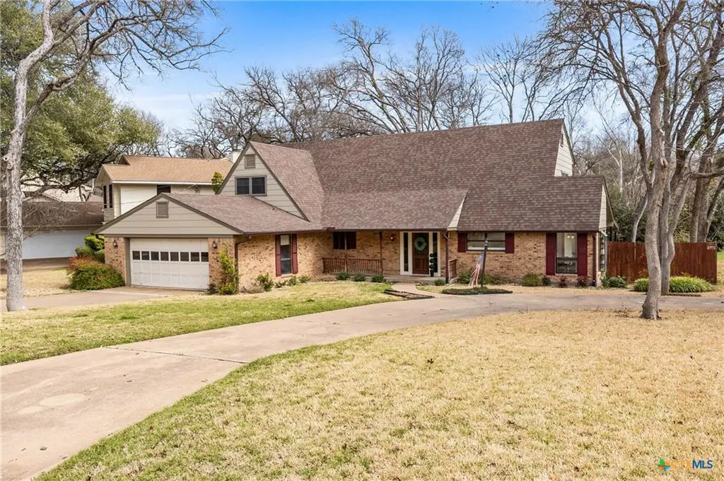 Brick 1980s traditional home with a two-car garage under mature trees in the Canyon Creek phases, Temple TX