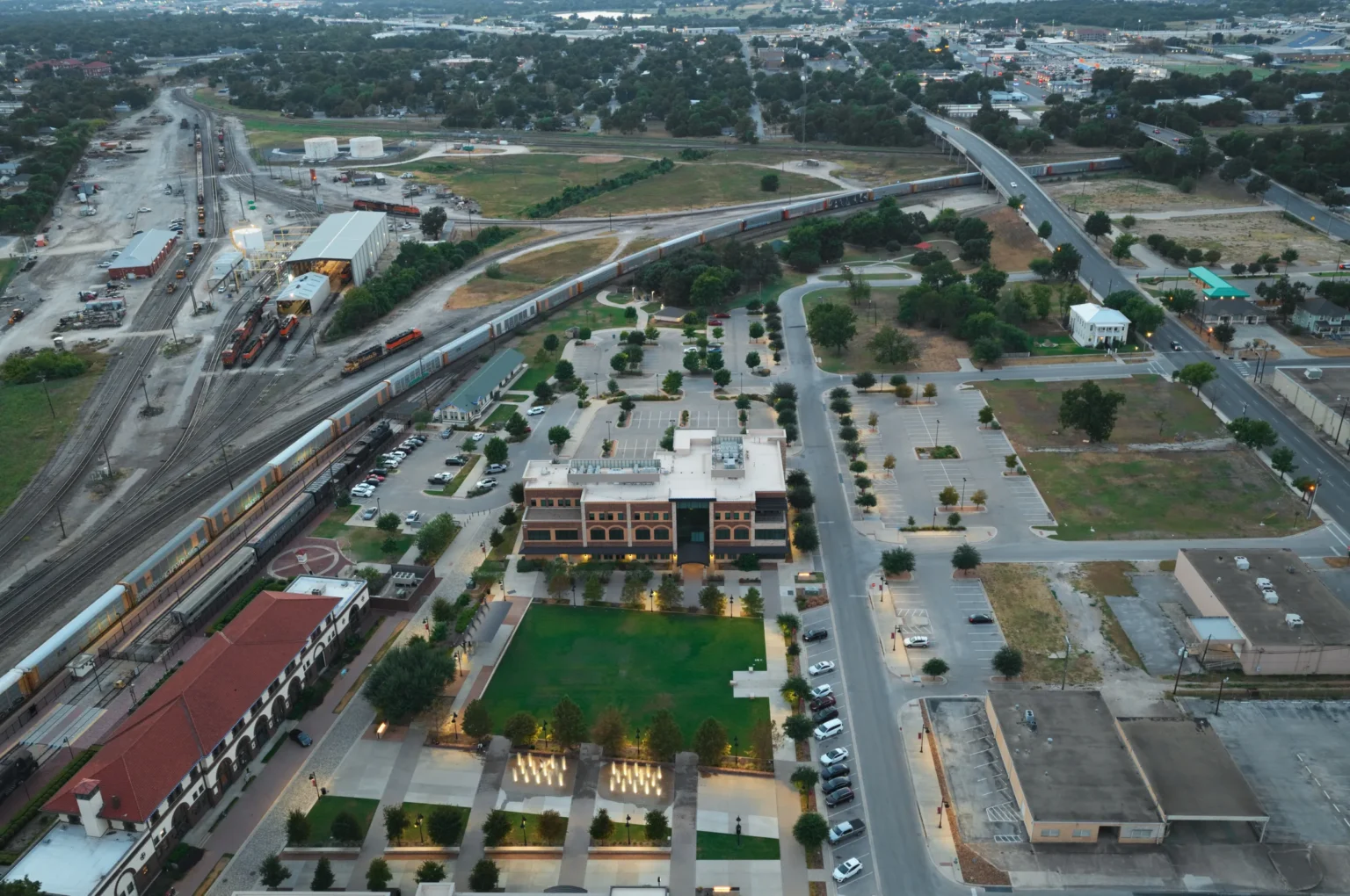 Santa Fe Plaza fountains, lawn and curving rail yard in downtown Temple, Texas, at dusk.