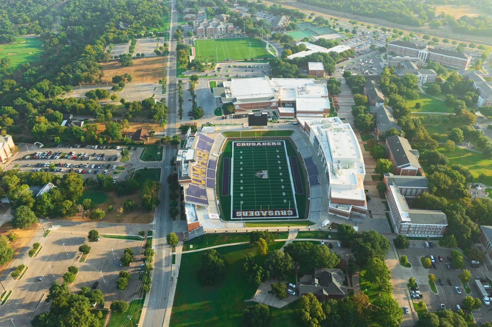 Morning aerial of UMHB’s football stadium in Belton, with purple and gold seating and surrounding campus.