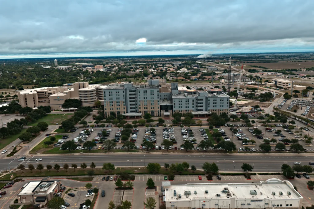 Aerial view of Baylor Scott & White Medical Center – Temple from across South 31st Street on an overcast evening, with the main parking lot between the road and the hospital