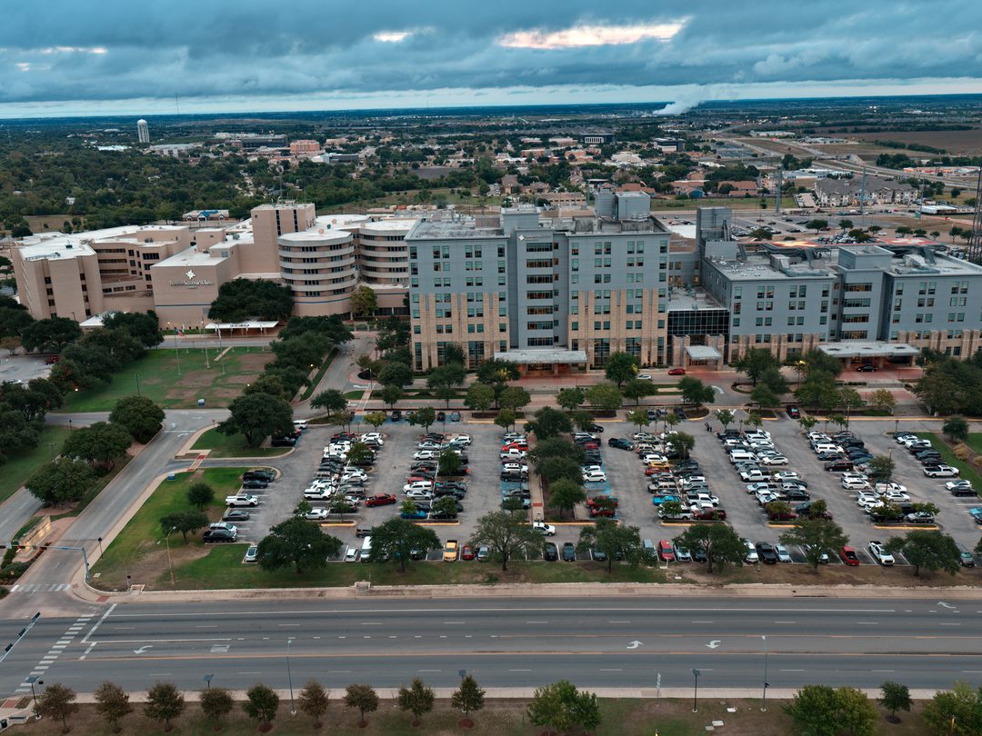 Aerial view of Baylor Scott & White Medical Center – Temple seen across South 31st Street under an overcast sky, with the hospital towers behind the main parking lot.