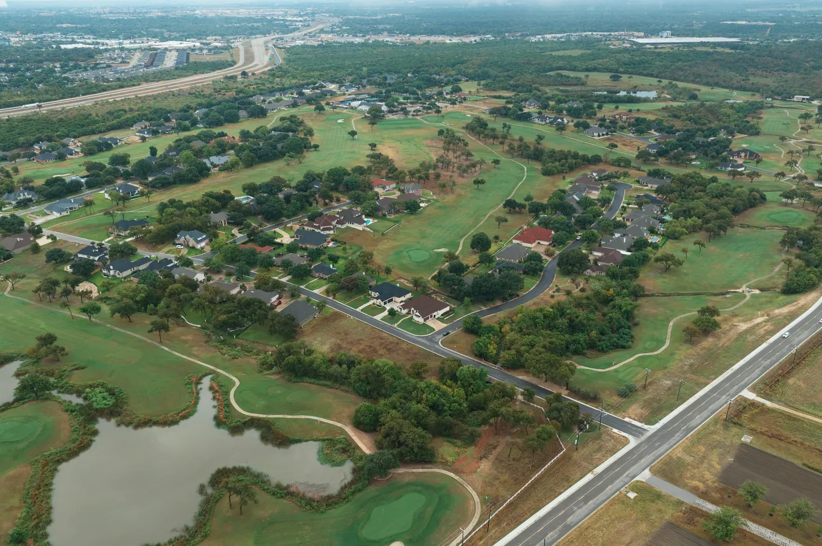 Wide aerial view of homes, winding streets, a pond and fairways in the Wildflower area.